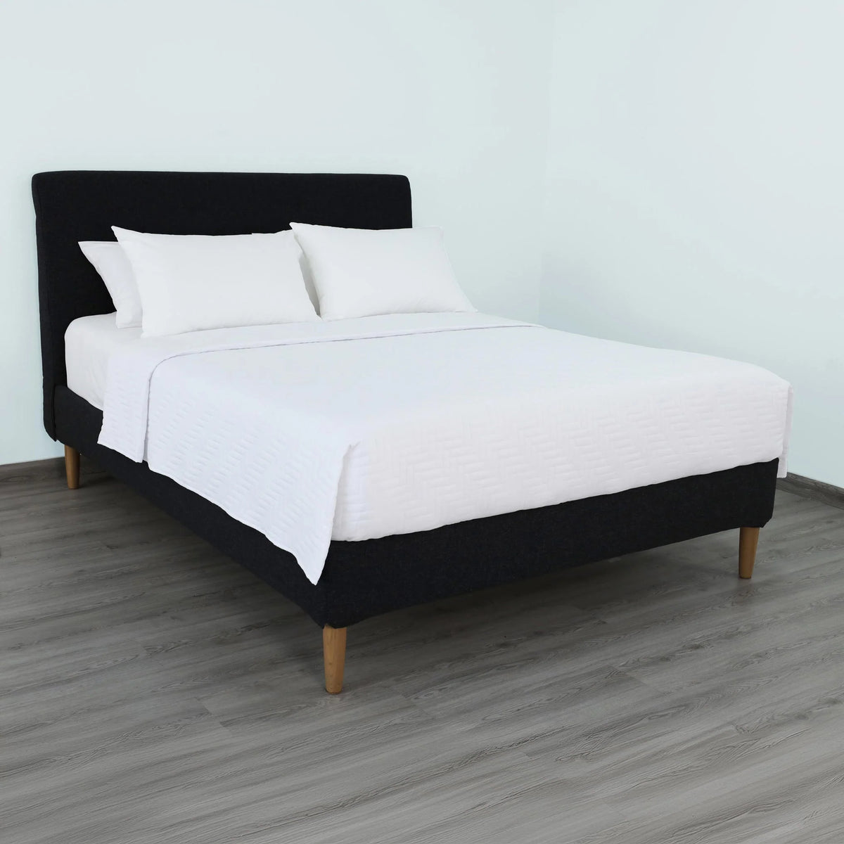 Pictured: Nicely made white bedding on a black fabric bedframe. The bed features the white Martex Suites Coverlet, which has a luxurious herringbone pattern.