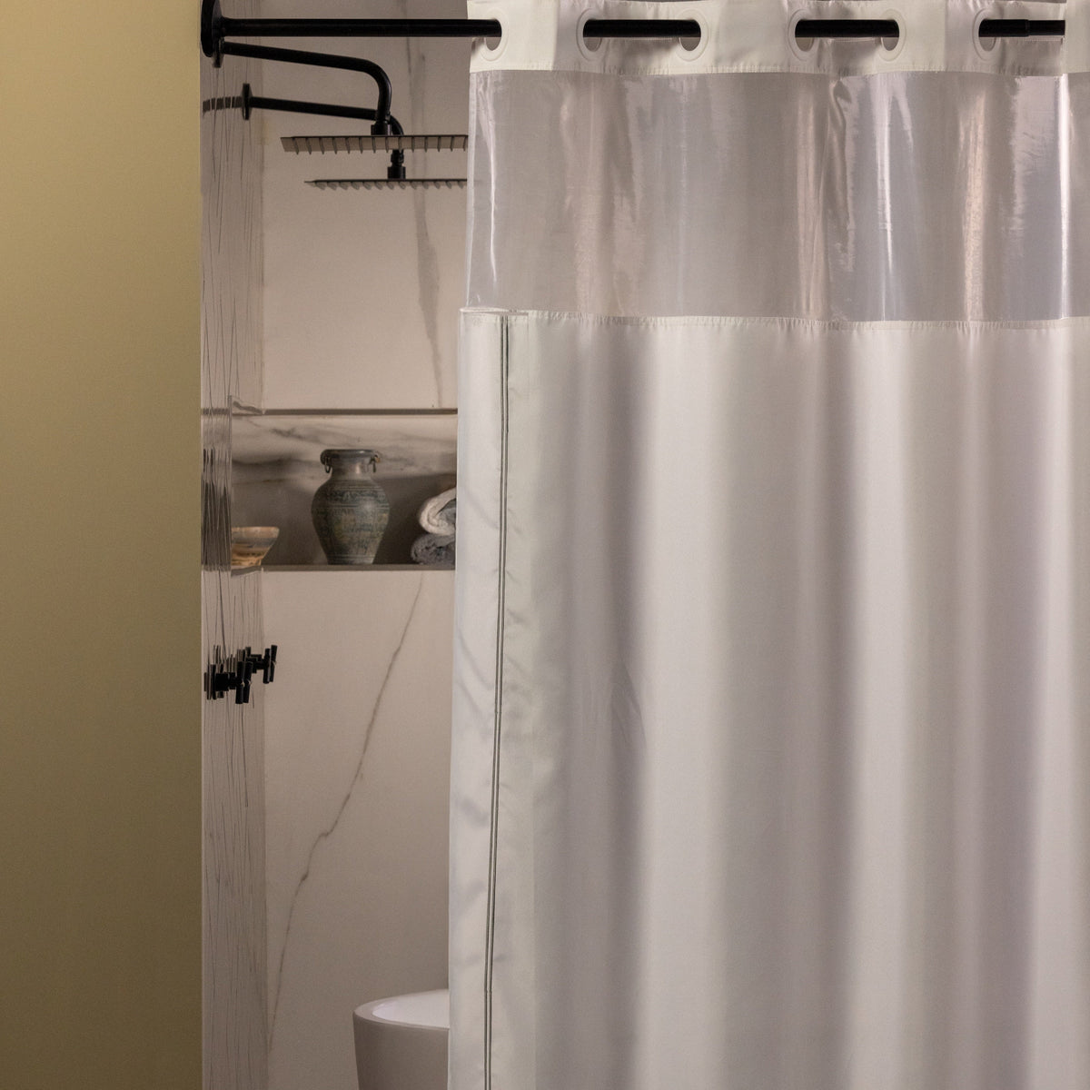 Pictured: Hookless Shower Curtain hanging from a black rod in a standing shower. The curtain is white with a clear window at the top. There are 2 thin black stripes that create a border around the curtain.