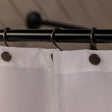 Close-up of a shower curtain with a black rod and hooks, featuring a neutral background.
