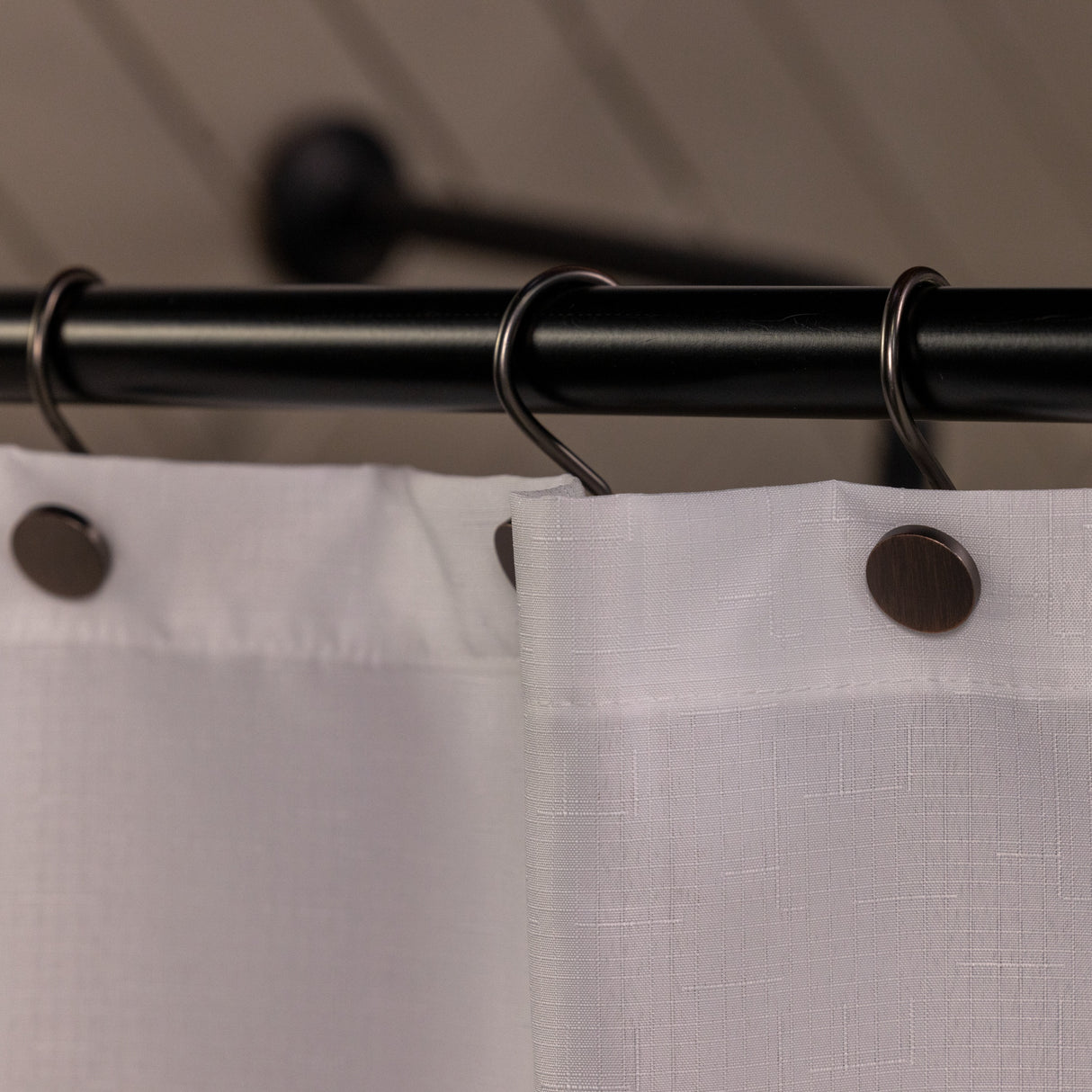Close-up of a shower curtain with a black rod and hooks, featuring a neutral background.