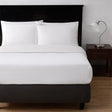 A bed showcasing a while top sheet and pillows. To the right is a nightstand with a lamp on top.