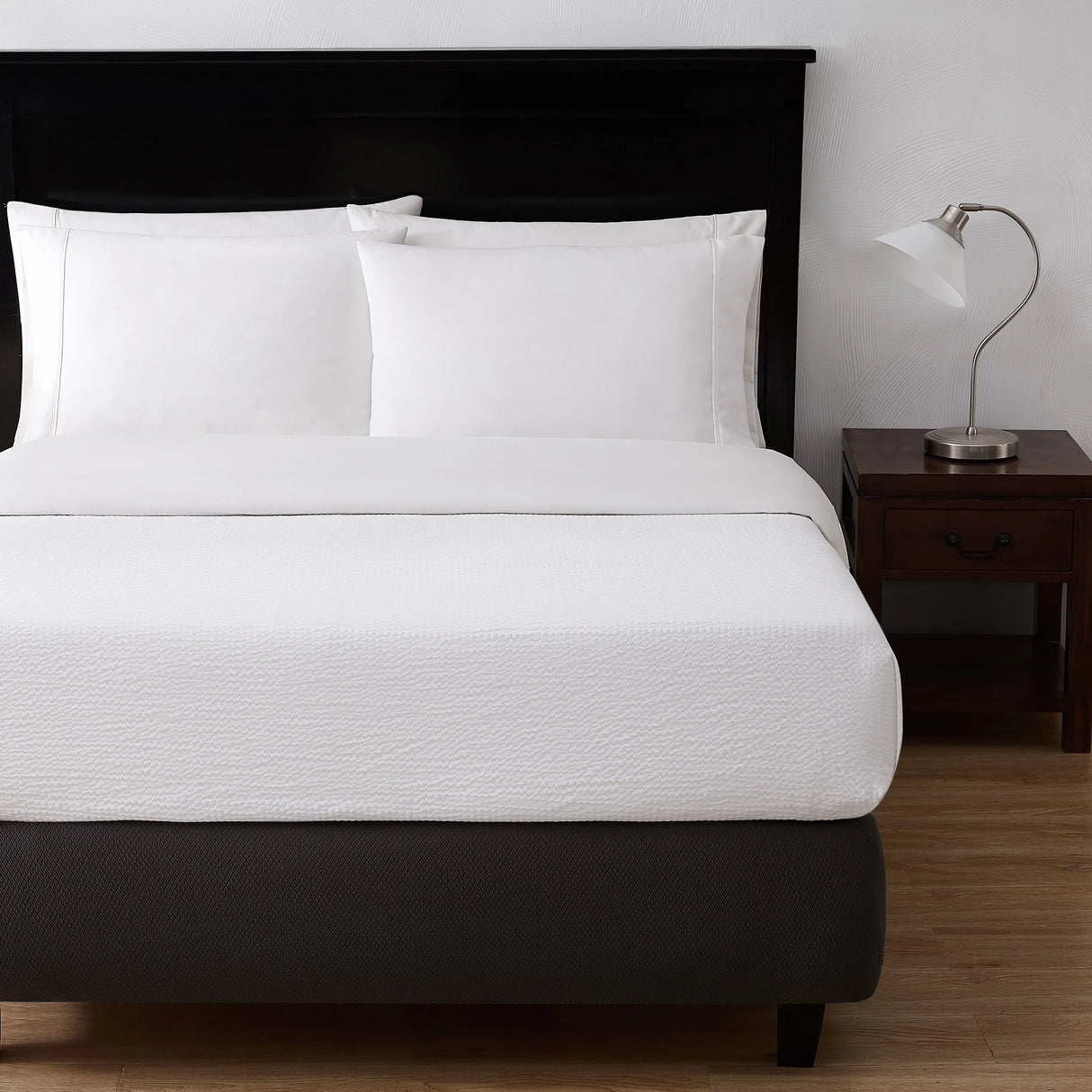 A bed showcasing a while top sheet and pillows. To the right is a nightstand with a lamp on top.