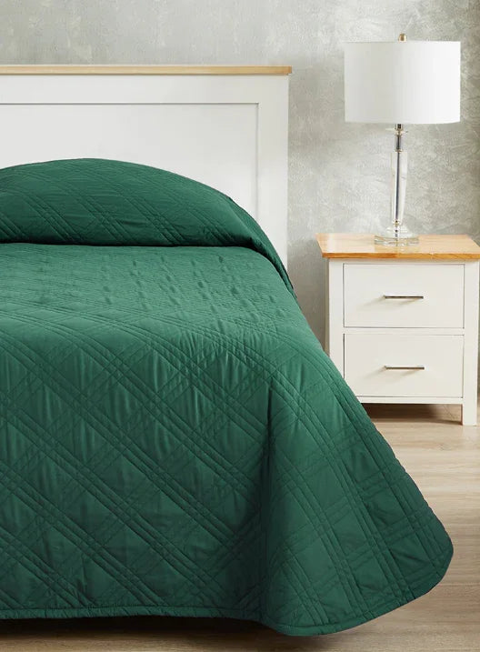 Forest green colored bedspread coverlet for single bed. Bed has white frame with wood detailing. Matching nightstand to the right with metal lamp on top.