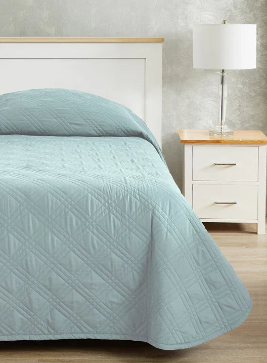Baby blue colored fitted coverlet for single bed. Bed has white frame with wood detailing. Matching nightstand to the right with metal lamp on top.