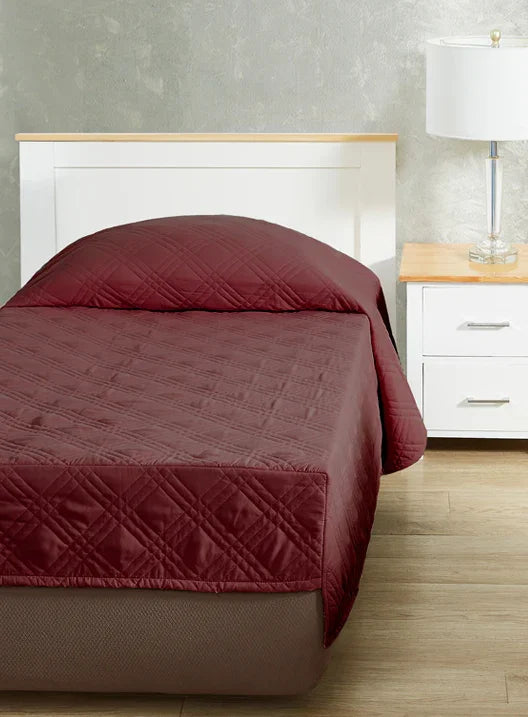Burgundy colored fitted coverlet for single bed. Bed has white frame with wood detailing. Matching nightstand to the right with metal lamp on top.