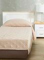 Beige colored fitted coverlet for single bed. Bed has white frame with wood detailing. Matching nightstand to the right with metal lamp on top.