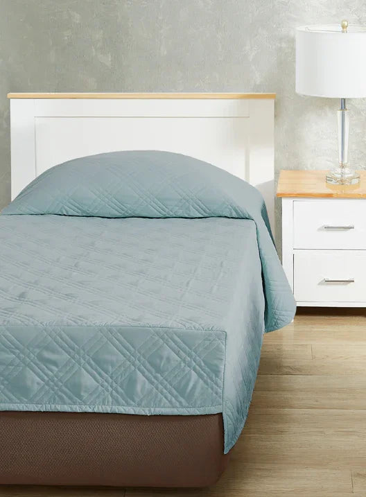 Teal blue colored fitted coverlet for single bed. Bed has white frame with wood detailing. Matching nightstand to the right with metal lamp on top.