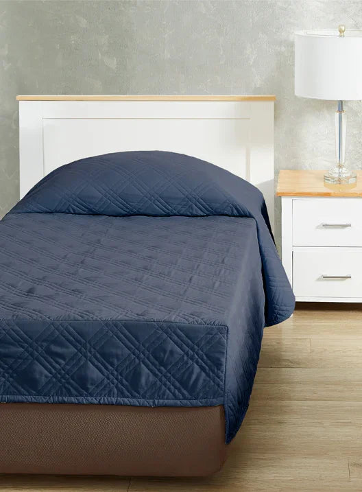 Navy blue colored fitted coverlet for single bed. Bed has white frame with wood detailing. Matching nightstand to the right with metal lamp on top.