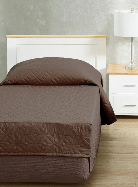 Cocoa brown colored bedspread coverlet for single bed. Bed has white frame with wood detailing. Matching nightstand to the right with metal lamp on top.