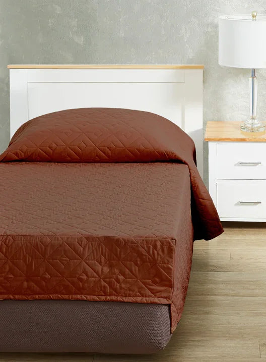 Redish Brown colored bedspread coverlet for single bed. Bed has white frame with wood detailing. Matching nightstand to the right with metal lamp on top.