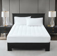 A white, plush mattress topper on a bed with two pillows, in a room with nightstands and lamps on either side of the bed.