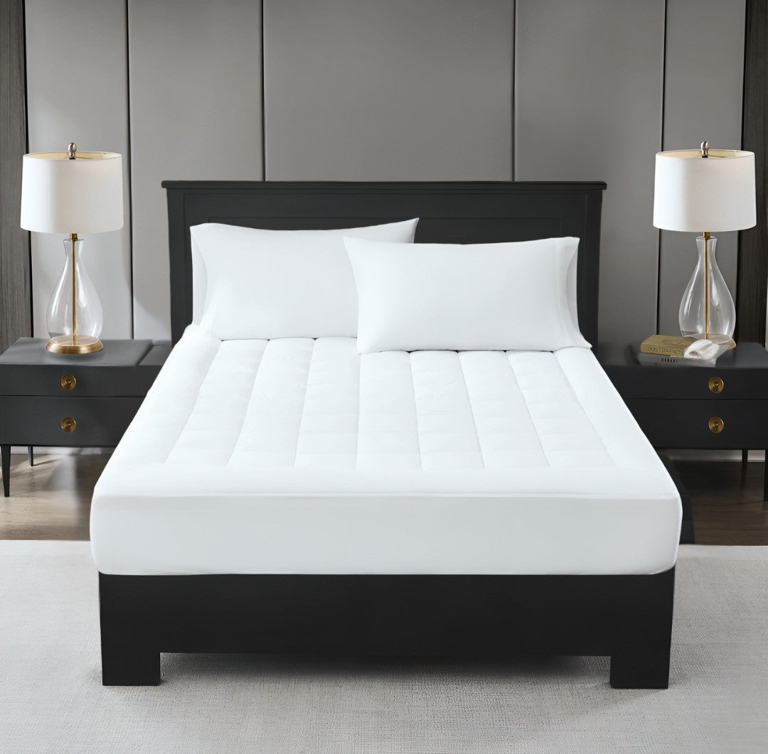 A white, plush mattress topper on a bed with two pillows, in a room with nightstands and lamps on either side of the bed.