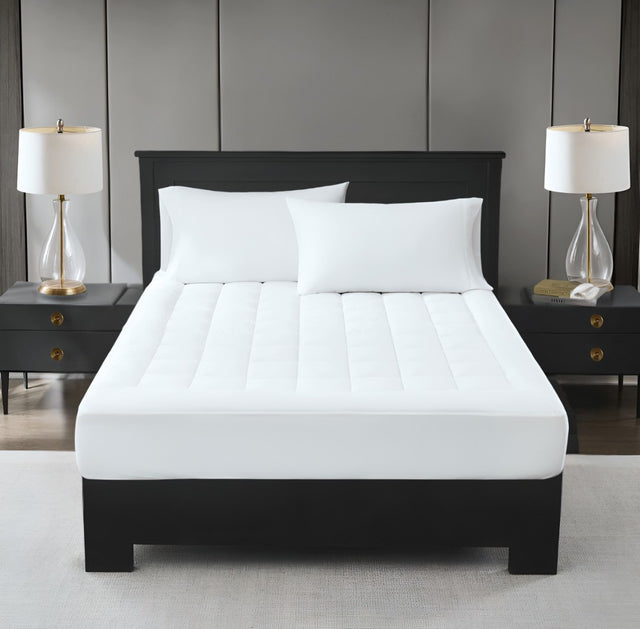 A white, plush mattress topper on a bed with two pillows, in a room with nightstands and lamps on either side of the bed.