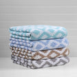 Product shot of diamond pattern towels in a variety of colors stacked on top of eachother. From top to bottom the colors include; teal, blue, brown and grey