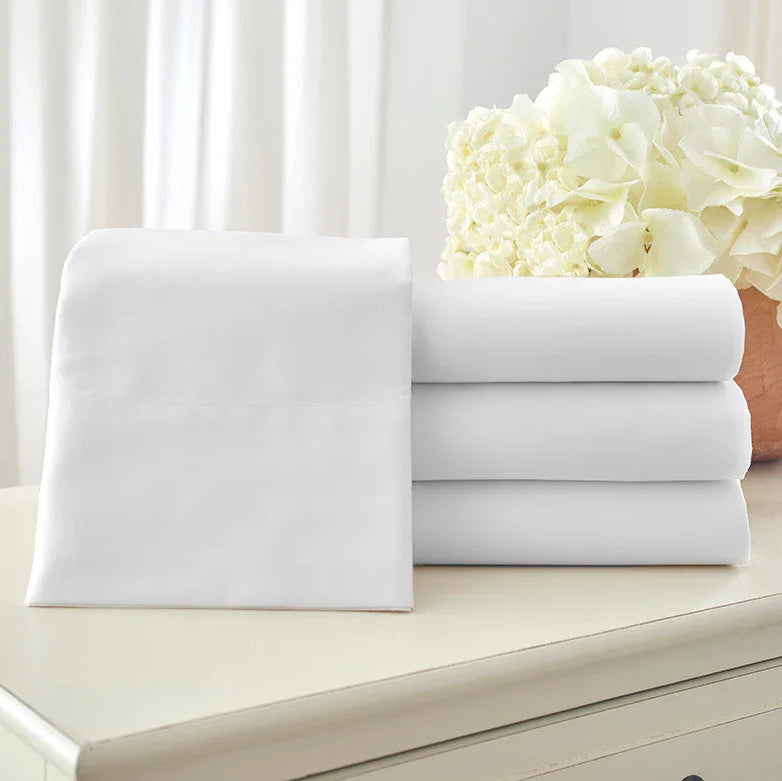 Pictured: Neatly folded white sheets sat atop a light wood surface. Three of the sheets are stacked, while one folded sheet is standing upright leaning against the stack.