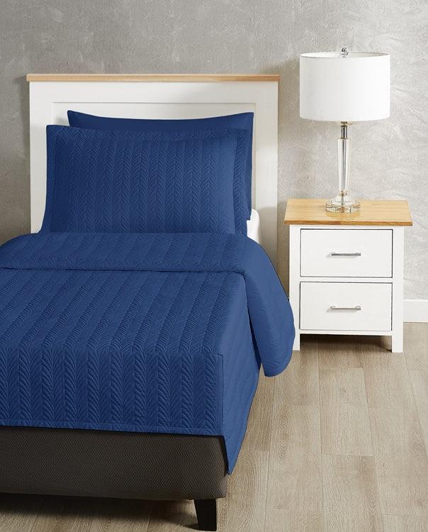 Dark blue colored bed sheet coverlet set for a single bed. White bedframe with wood detailing. Matching nightstand with metal lamp on top.