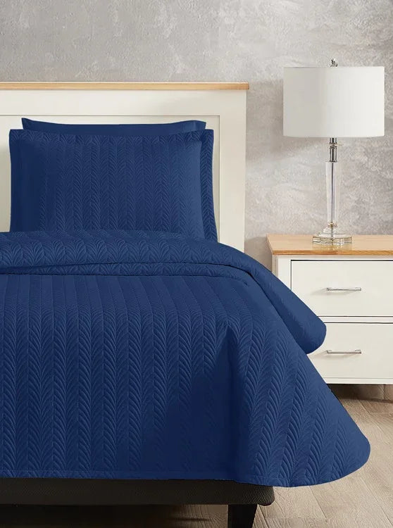Dark blue colored bed sheet coverlet set for a single bed. White bedframe with wood detailing. Matching nightstand with metal lamp on top.