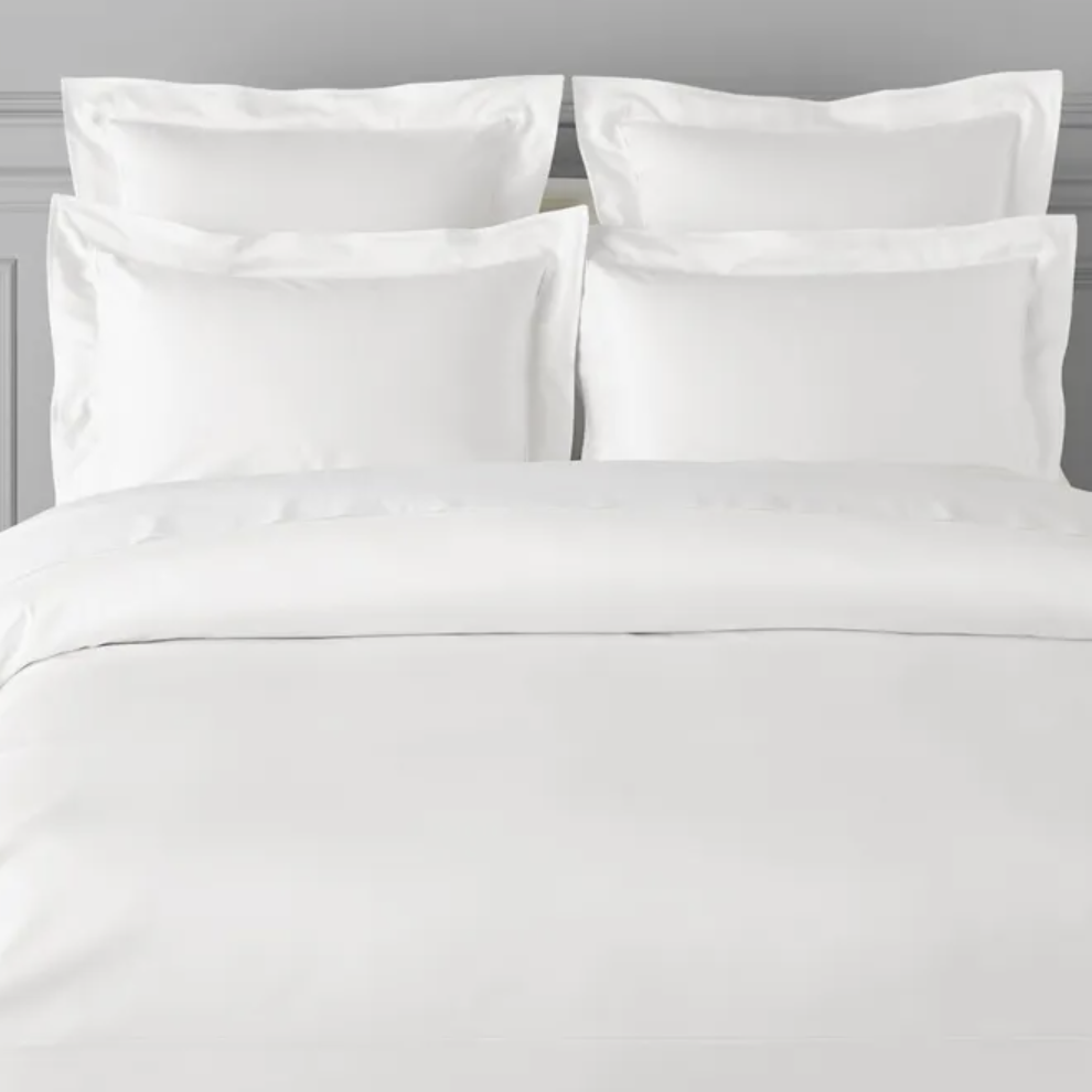 Pictured: Nicely made white bed with fluffy pillows against a gray wall. The product featured is the Georgetown Duvet Cover by Garnier Thiebaut.