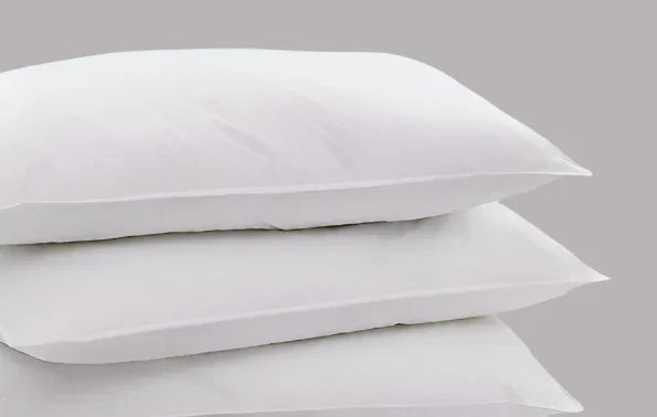 Product shot of 3 white fluffy pillows stacked on top of each other. The background is a gray color.
