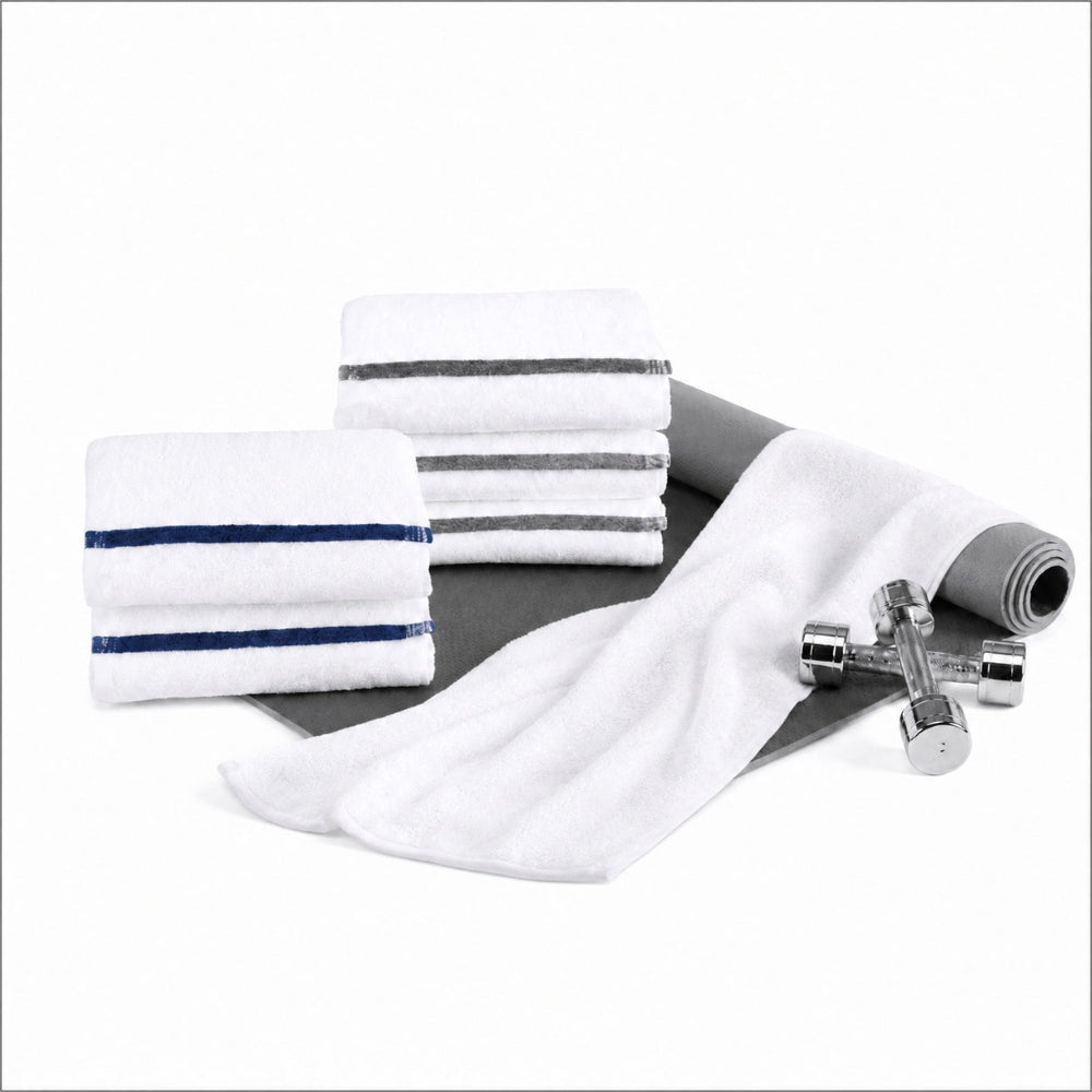 Pictured: Two stacks of white folded towels, one with grey stripes and one with blue stripes. They are sitting on top of a semi-rolled yoga mat, which has a white towel draped over it and two weights to the right. All of this is against a white background.
