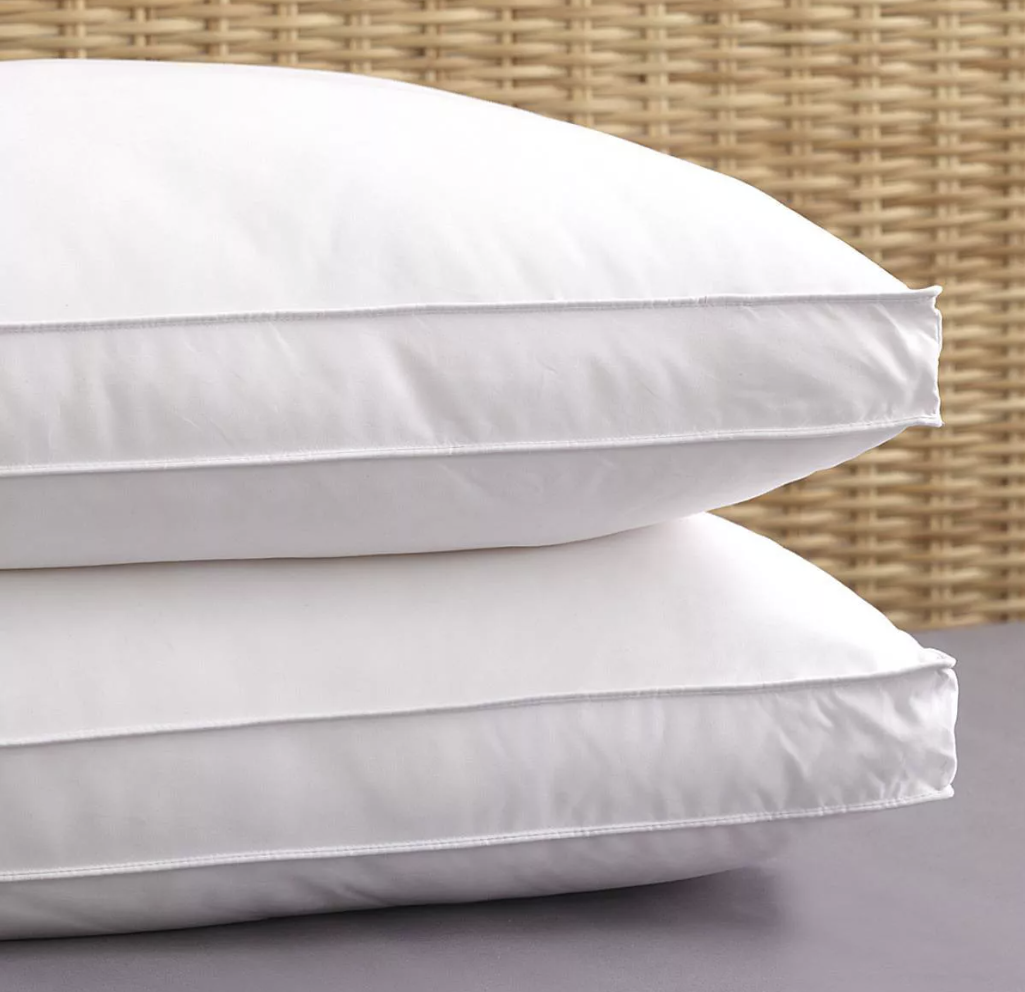 Two white pillows with gusseted sides placed on a surface with a woven object in the background.