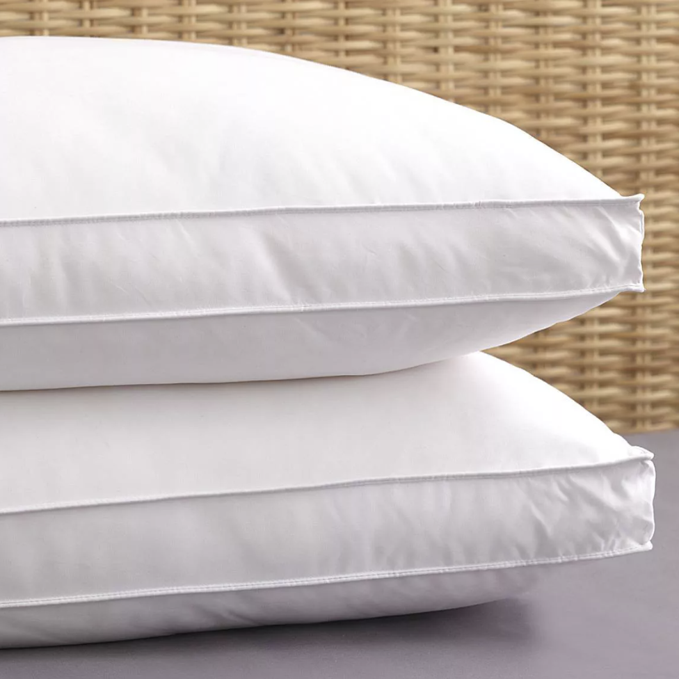 Pictured: Two white Luxurious Dream Pillows stacked on top of a grey counter and in front of a natural wicker background.
