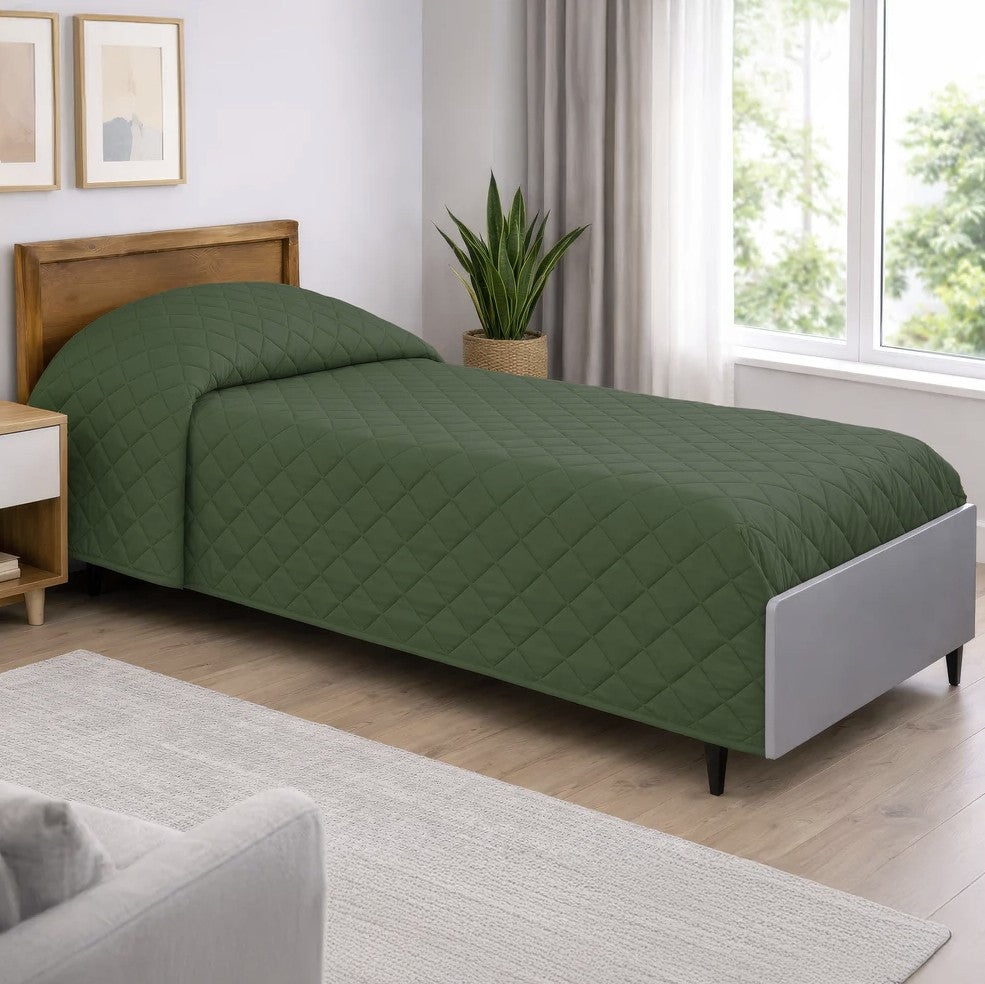 Green quilted bedspread on a bed in a well-lit bedroom with a window and plant.