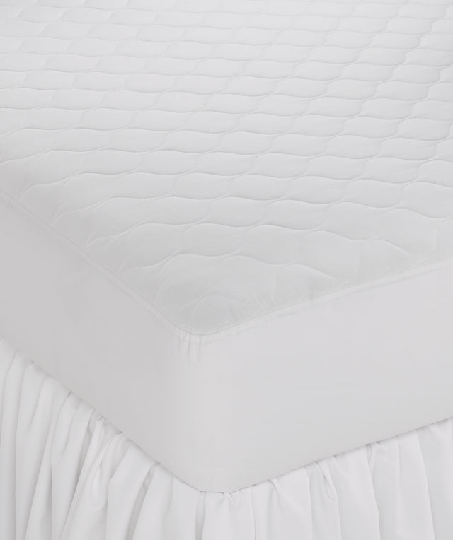 A white, fitted Martex Ultra Touch Mattress Pad on a bed, showcasing its quilted design and fitted skirt.