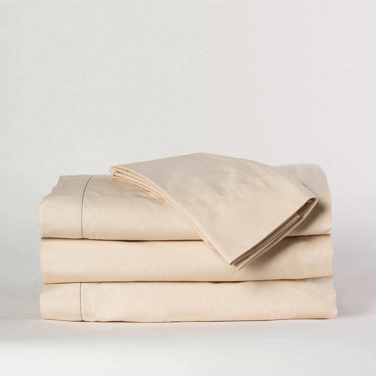 A stack of beige percale bed sheets made from a blend of cotton and polyester, displayed against a neutral background.