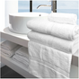 White towels neatly folded and placed on a shelf with a white sink and mirror in the background, showcasing a clean and elegant look.