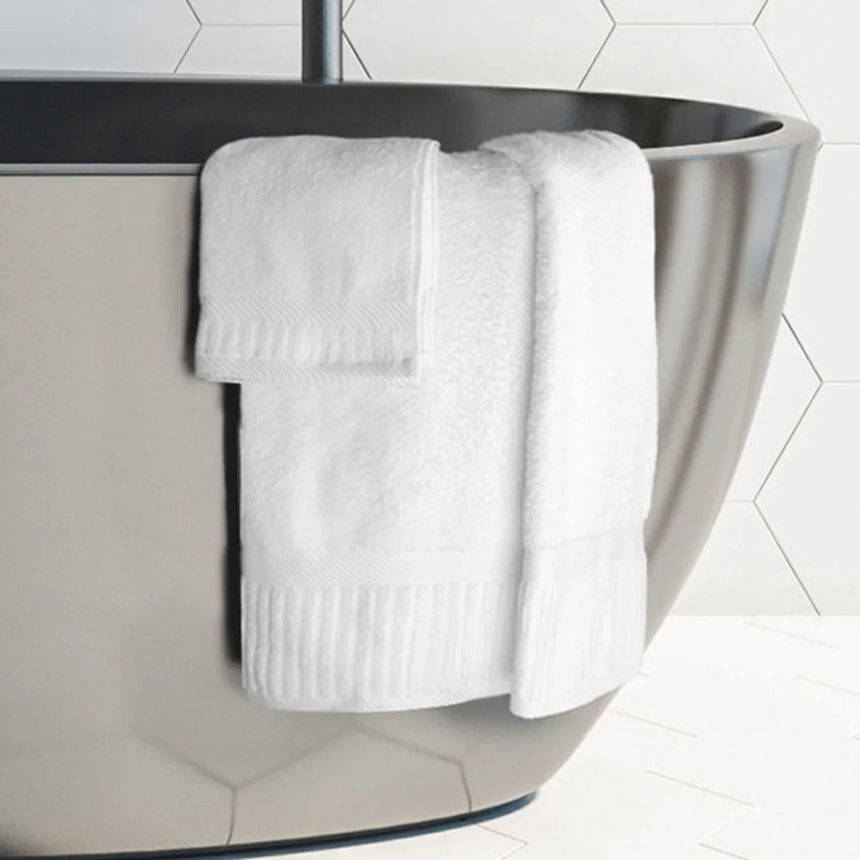 Product shot of the oxford signature towel collection. White fluffy towel hanging off the edge of a mirrored bathtub. Features hand towel and bath towel.