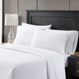 A set of white PureRest bed sheets displayed on a bed, with a lamp and a nightstand in the background.