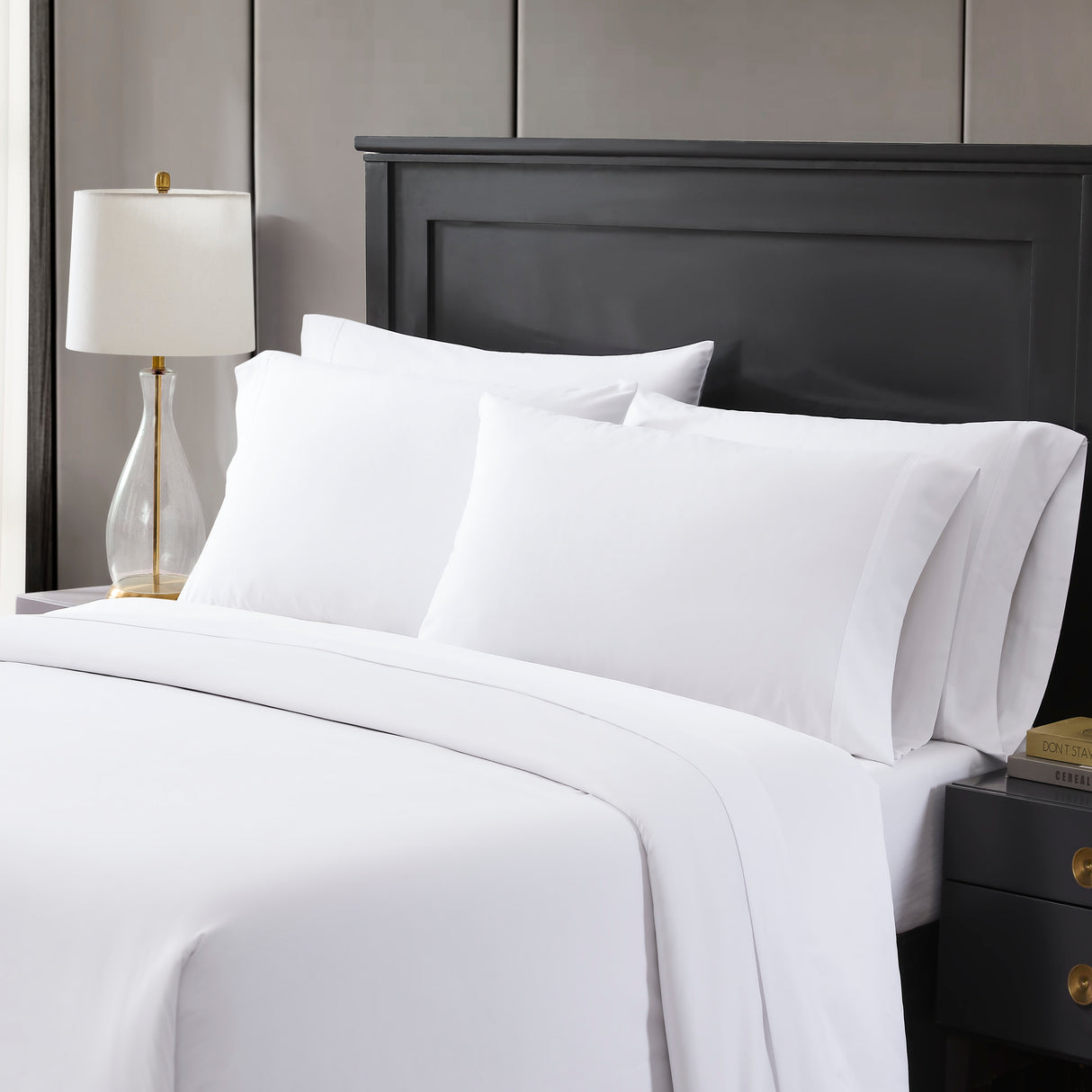 A set of white PureRest bed sheets displayed on a bed, with a lamp and a nightstand in the background.