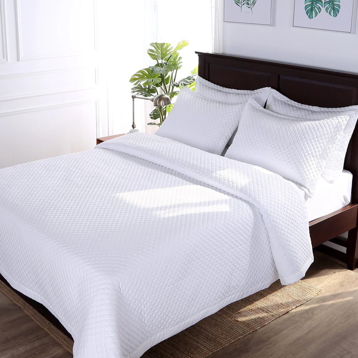 Diamond coverlet for bed in wholesale supply by Boston Textile Co. Photo shows the sheets on top of a bed with fluffy pillows and a plant in the background.