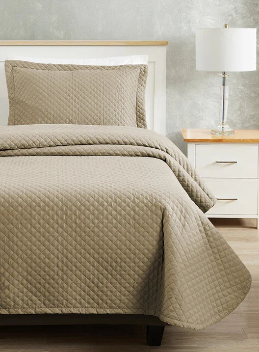 Light brown colored bed sheet coverlet set for a single bed. White bedframe with wood detailing. Matching nightstand with metal lamp on top.