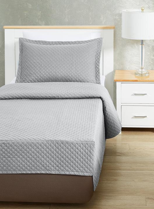 grey colored bed sheet coverlet set for a single bed. White bedframe with wood detailing. Matching nightstand with metal lamp on top.