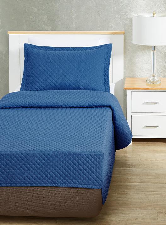 Blue colored bed sheet coverlet set for a single bed. White bedframe with wood detailing. Matching nightstand with metal lamp on top.