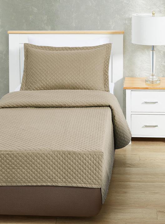 Light brown colored bed sheet coverlet set for a single bed. White bedframe with wood detailing. Matching nightstand with metal lamp on top.