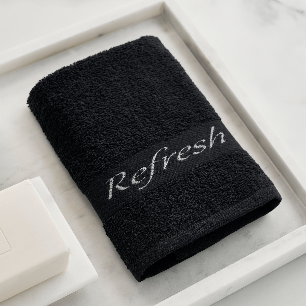 Black towel with 'Refresh' embroidery on a marble surface
