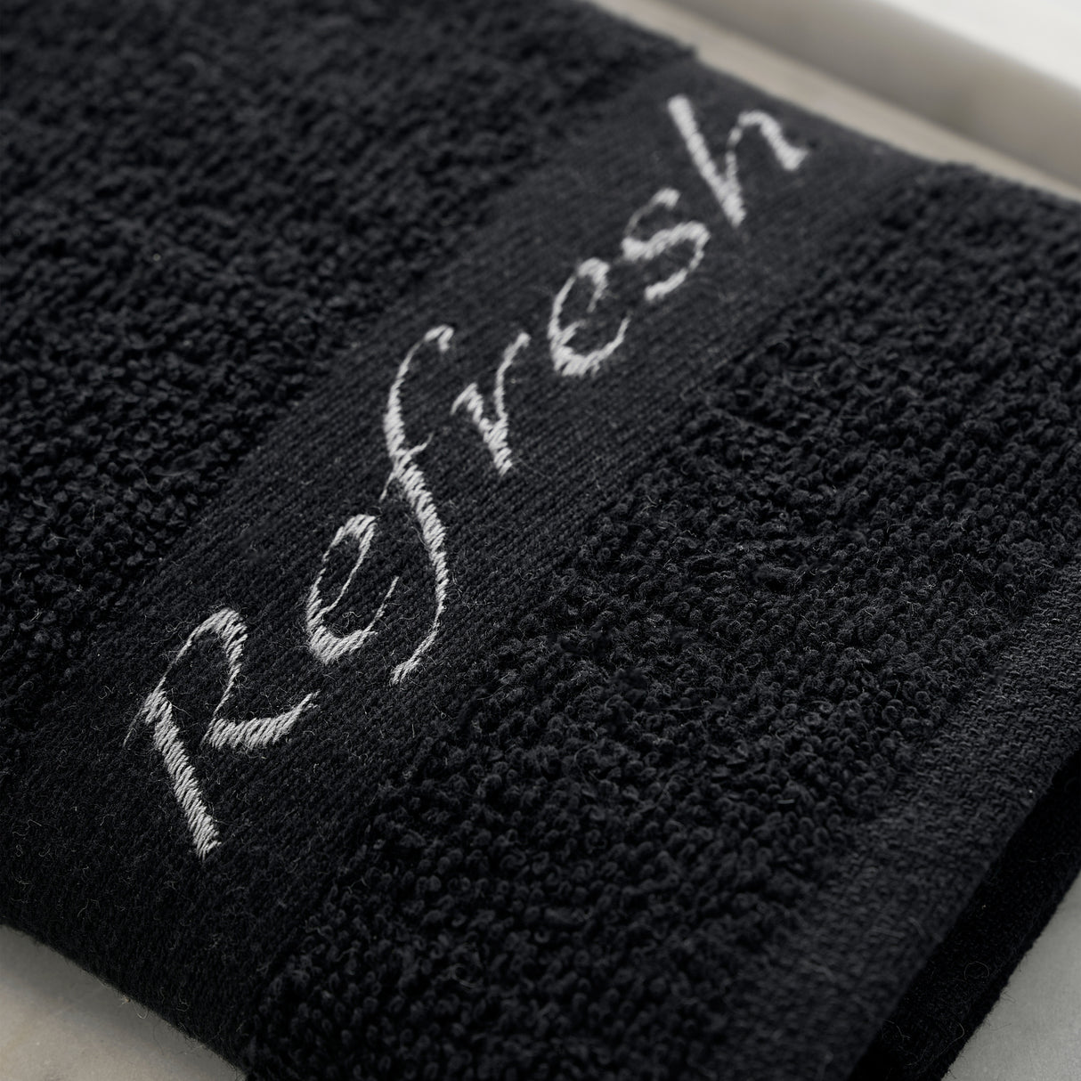 Black towel with 'Refresh' embroidery on a white surface