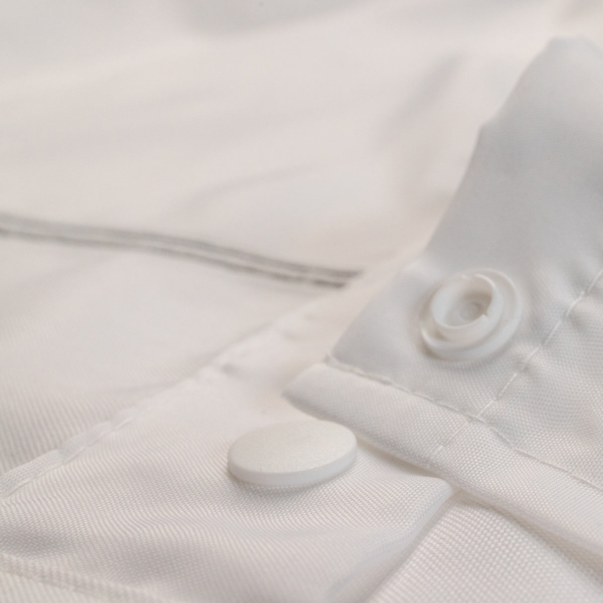 Close-up of a white textured fabric with buttons and a zipper.