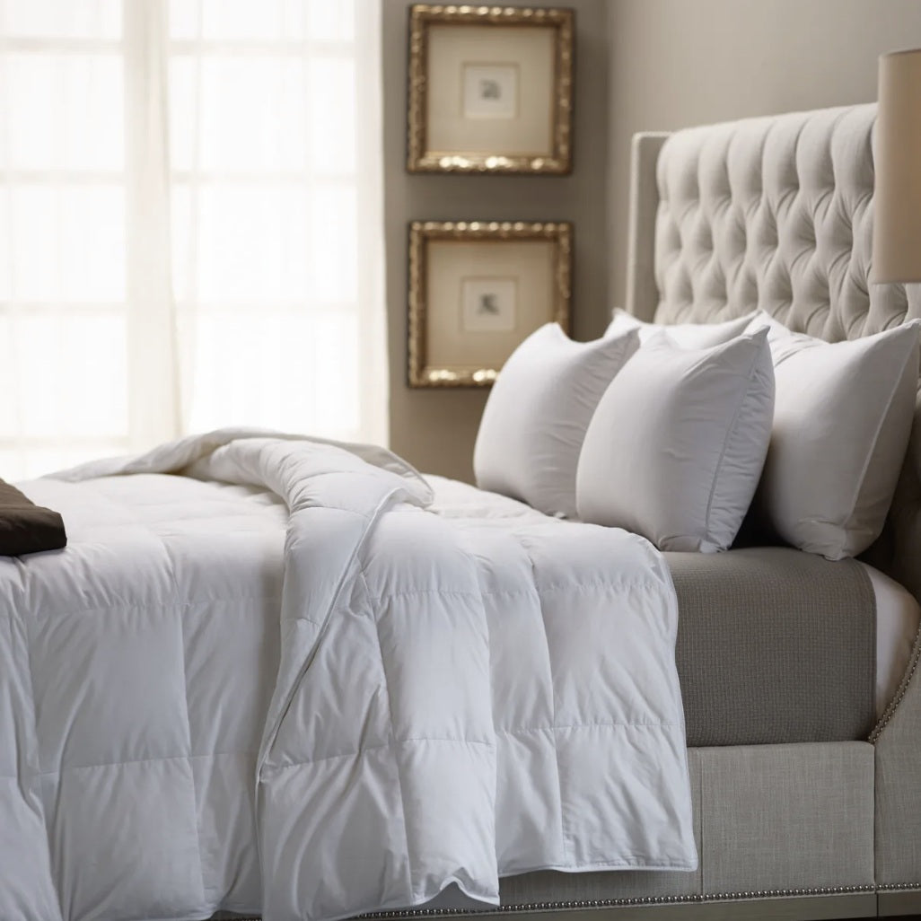 Neatly made bed with white bedding and gray headboard in a bedroom setting.
