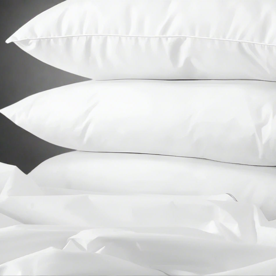 Pictured: Three white pillows stacked on top of each other. They sit in front of a grey background on top of some scrunched up white sheets.