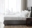 Side view of a bed showcasing a top sheet with pillows near a window overlooking a metropolitan city.