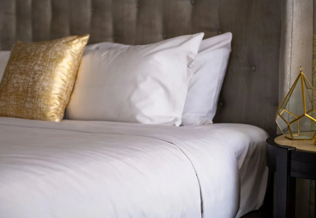 Photoshoot showcases bed with fluffy pillows and decorative pillows in a gold color.