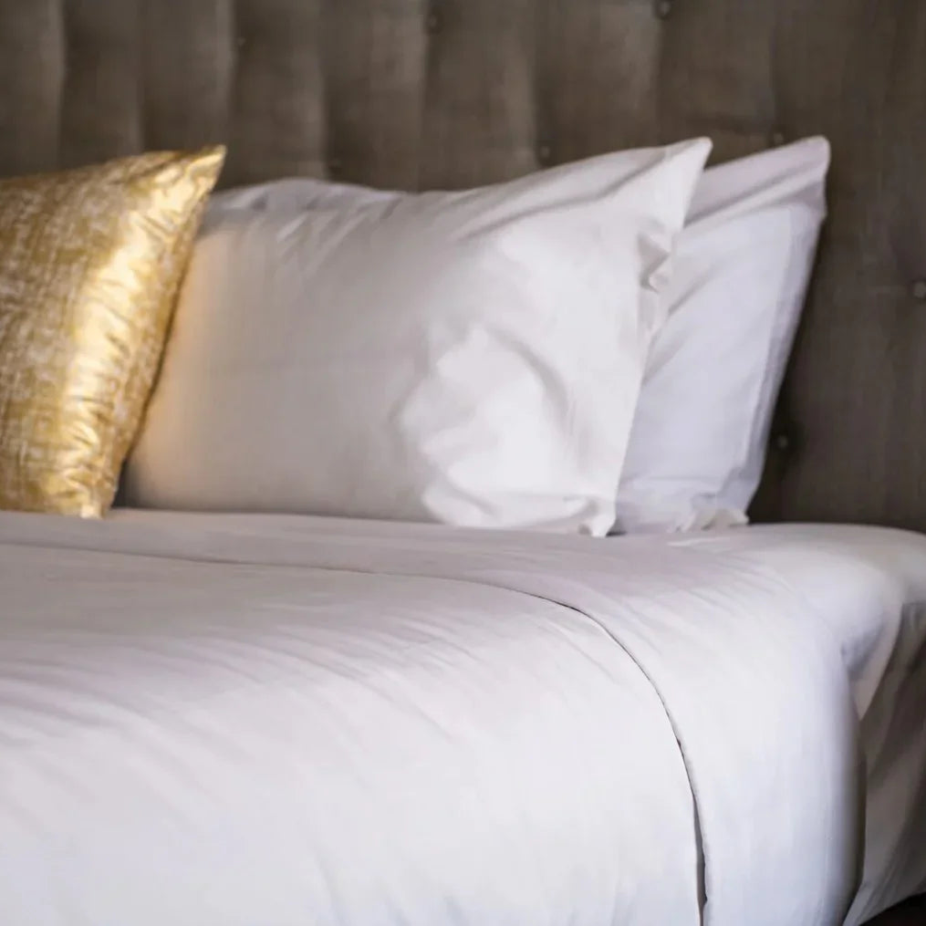 Pictured: White bedding against a grey fabric headboard. There is a gold accent pillow on the bed as well.