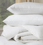 A stack of white duck feather and down pillows with a cotton shell on a bed.