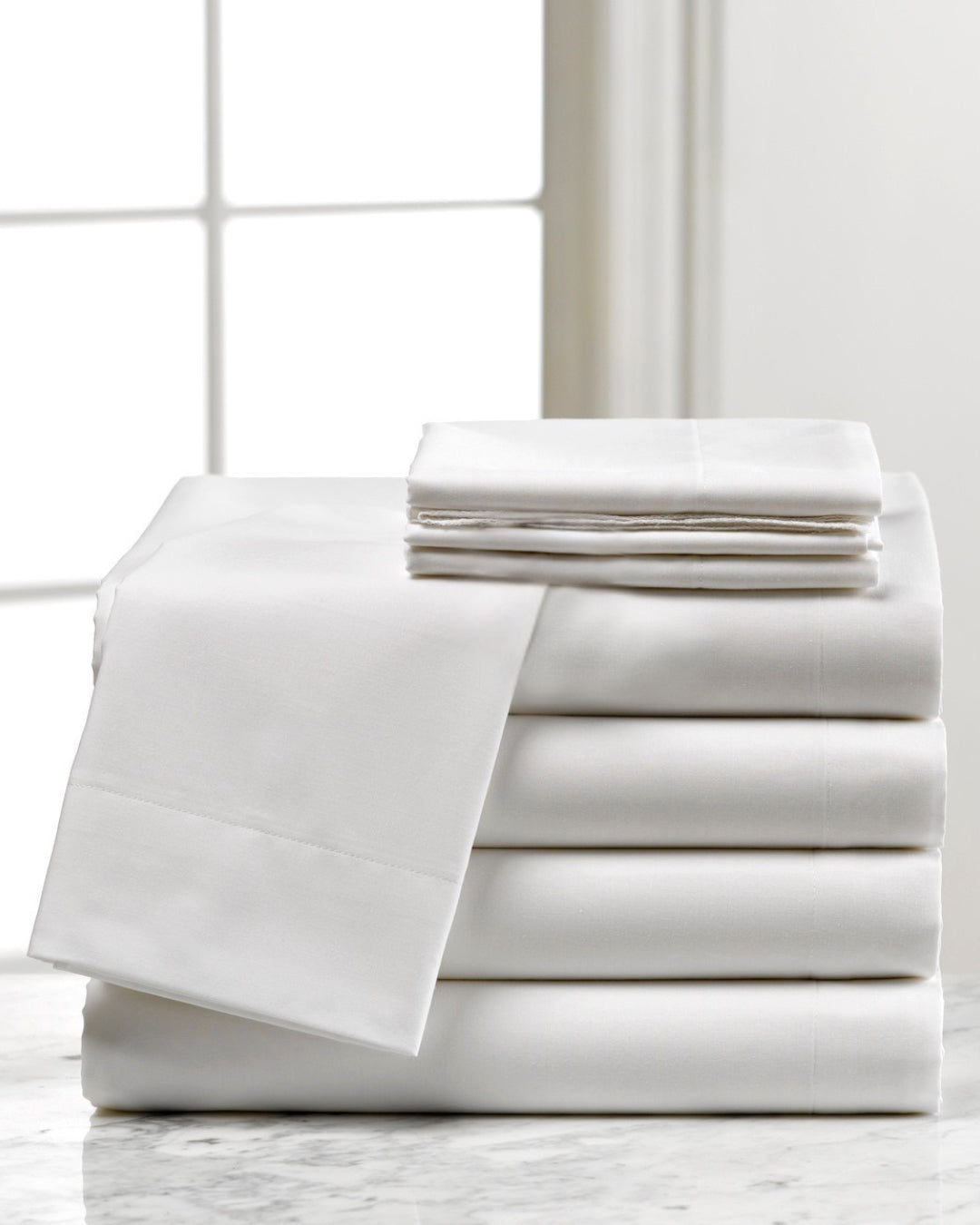 Stack of white folded sheets on a marble surface with a window in the background