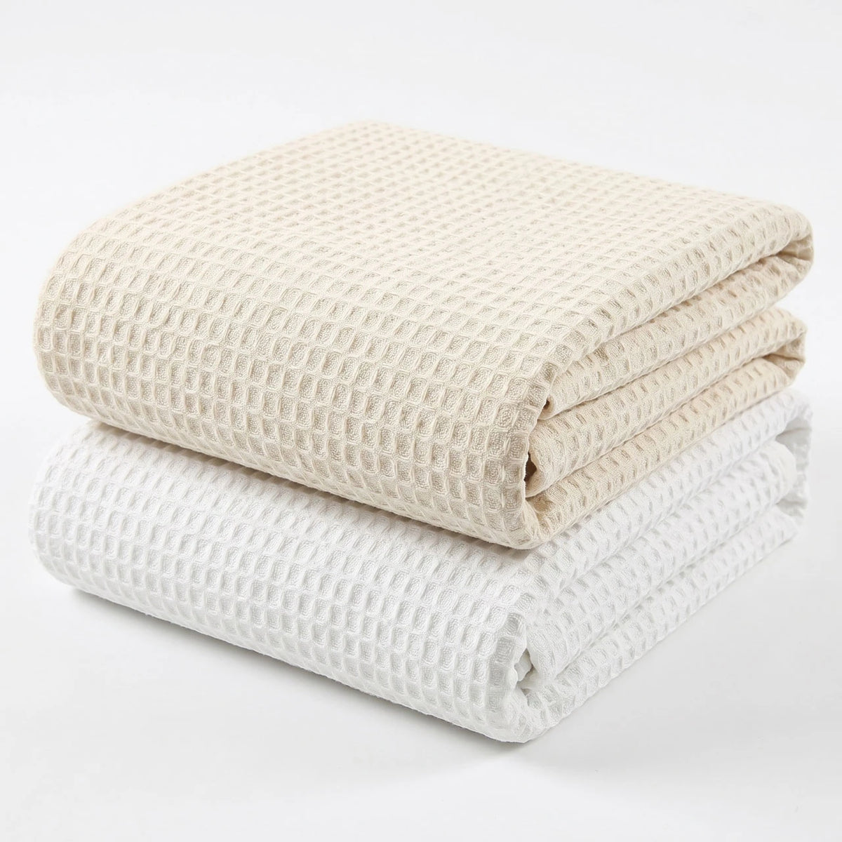 Pictured: Two waffle woven blankets neatly folded and stacked against a white background. The blanket on the bottom is in the shade "White" and the one on top is in the shade "Beige".