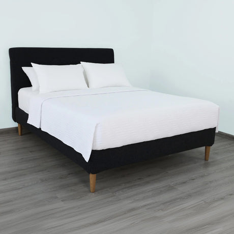 Pictured: Nicely made white bedding on a black fabric bedframe. The bed features the white Martex Suites Coverlet, which has a luxurious herringbone pattern.